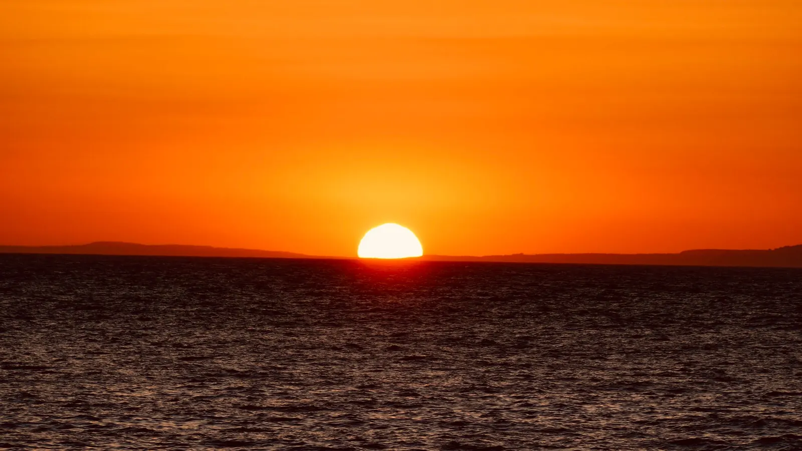 Bright sun rising over the ocean under a vivid orange sky
